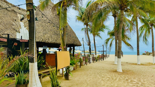 A sandy beach with palm trees and a thatched roof
